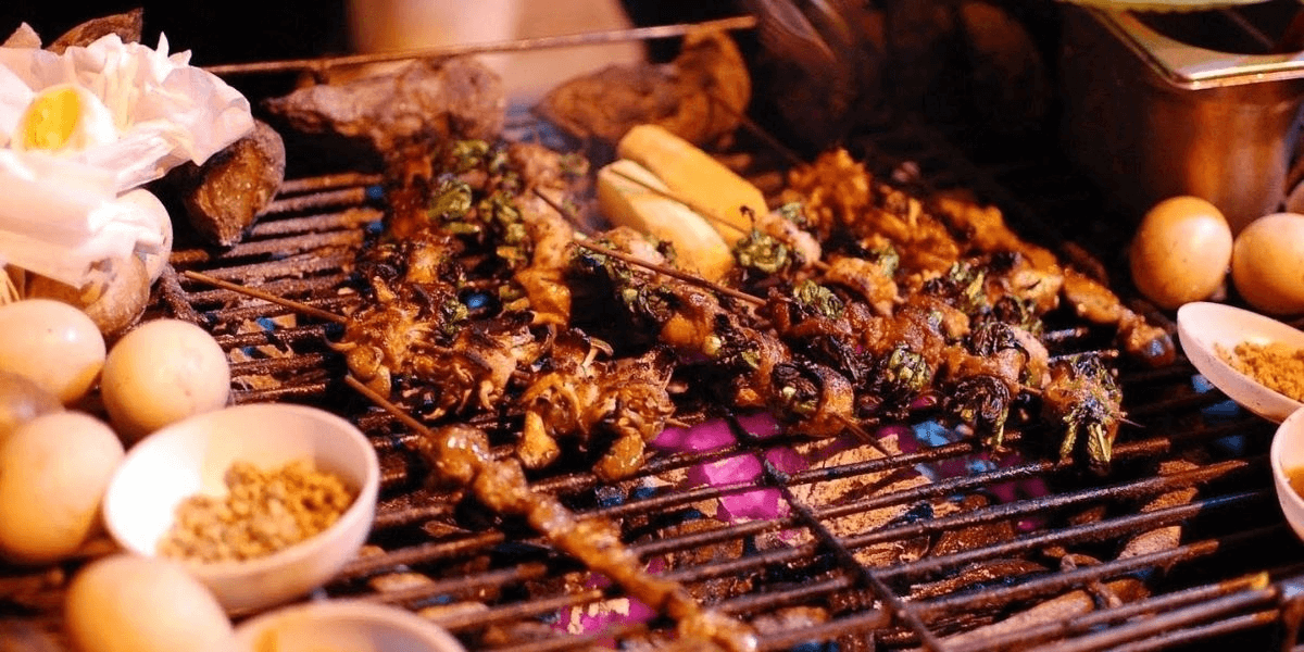 An array of marinated meats, fresh vegetables, and regional specialties over open flames (Source: Threeland Travel)
